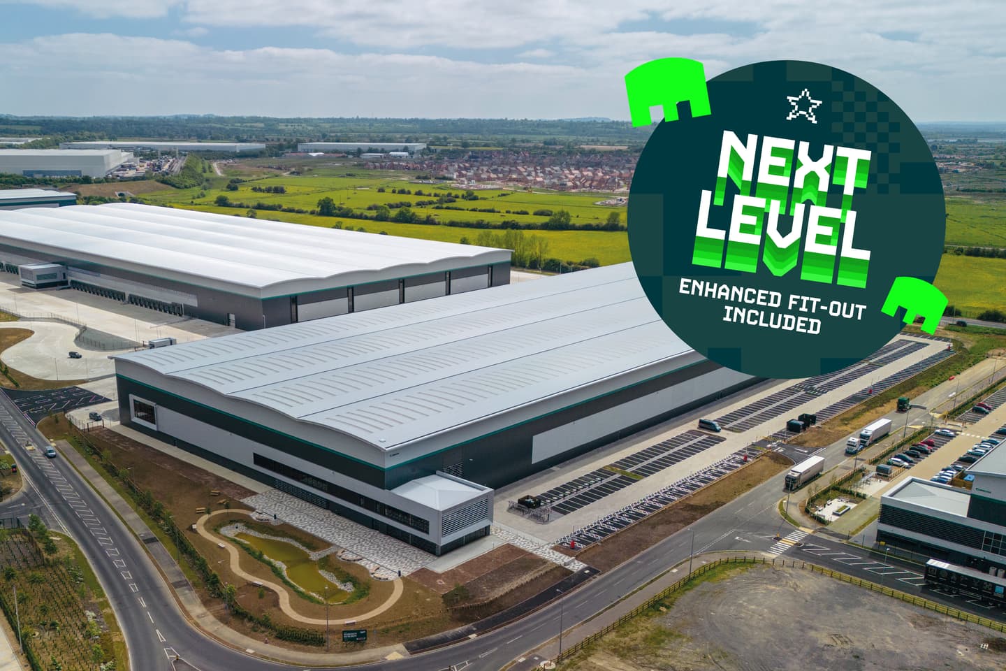A large warehouse facility with parking spaces and surrounding roads, featuring a circular graphic stating NEXT LEVEL ENHANCED FIT-OUT INCLUDED.
