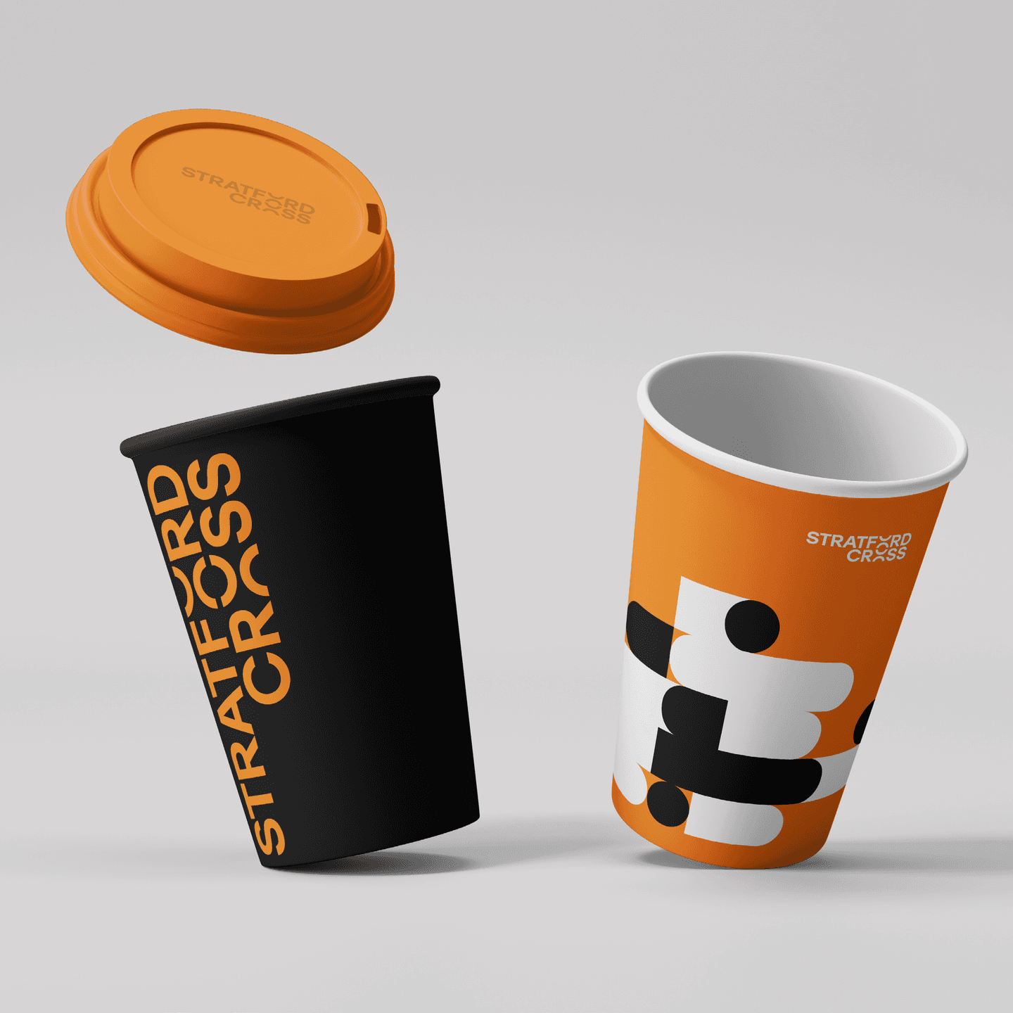 Two branded coffee cups and an orange lid are shown. One cup is black with vertical STRATFORD CROSS text, and the other is orange with abstract black and white shapes and a small logo.