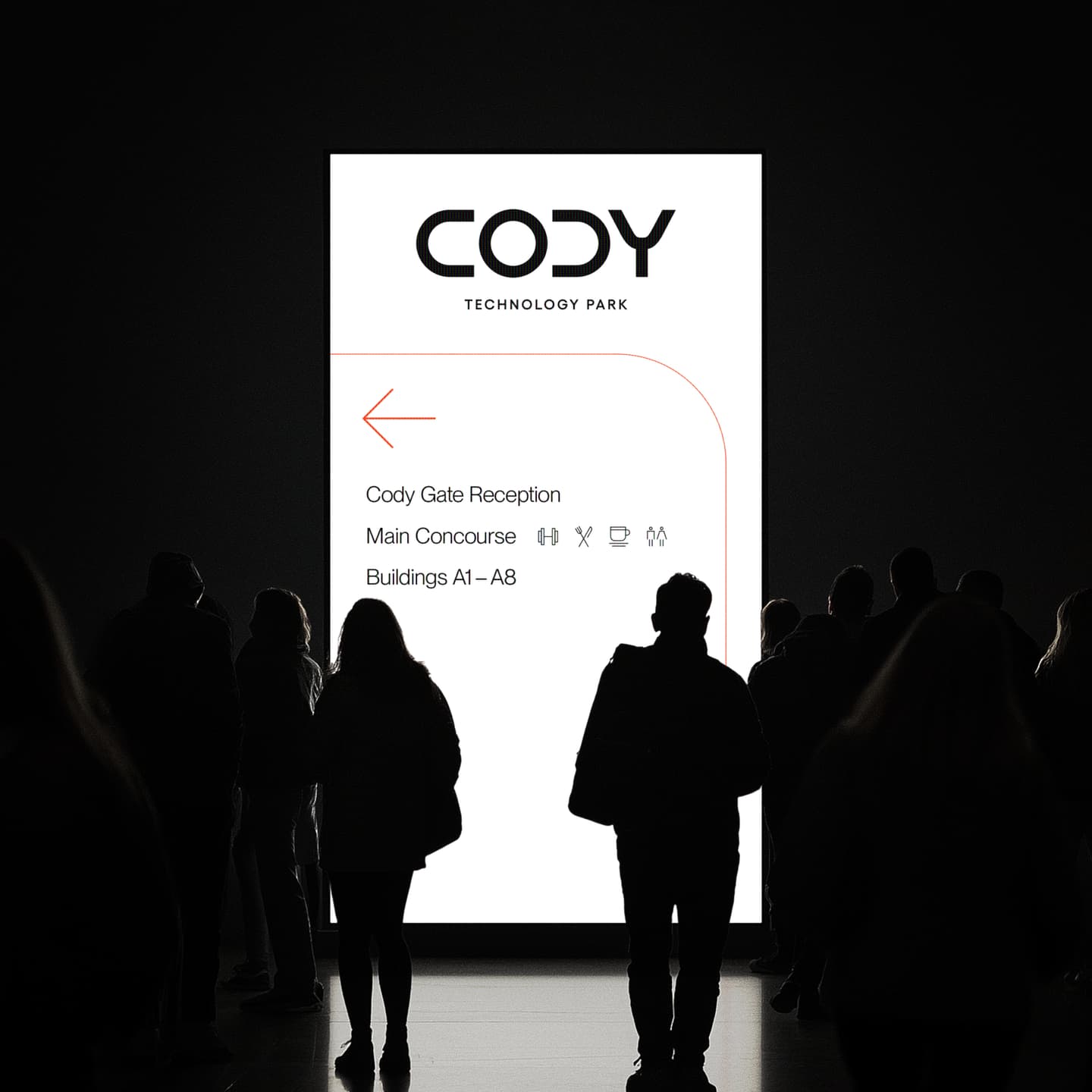 A group of people stands in front of a large illuminated directory sign for Cody Technology Park, displaying directions to the Cody Gate Reception, Main Concourse, and Buildings A1–A8.
