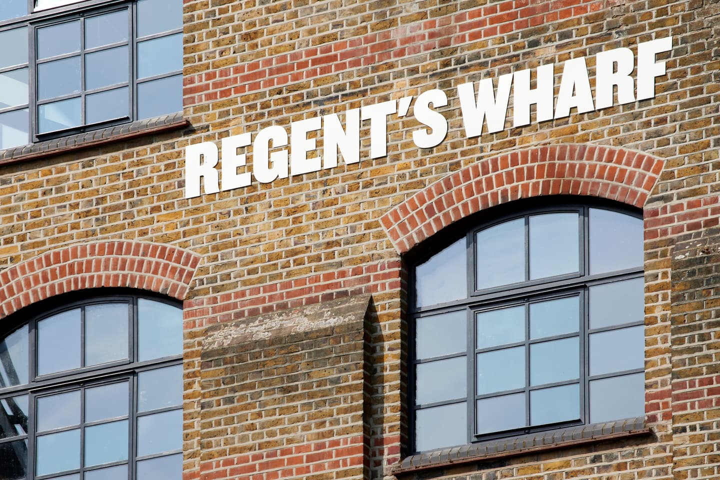 A brick building with arched windows and the words REGENTS WHARF in large white letters on the wall.