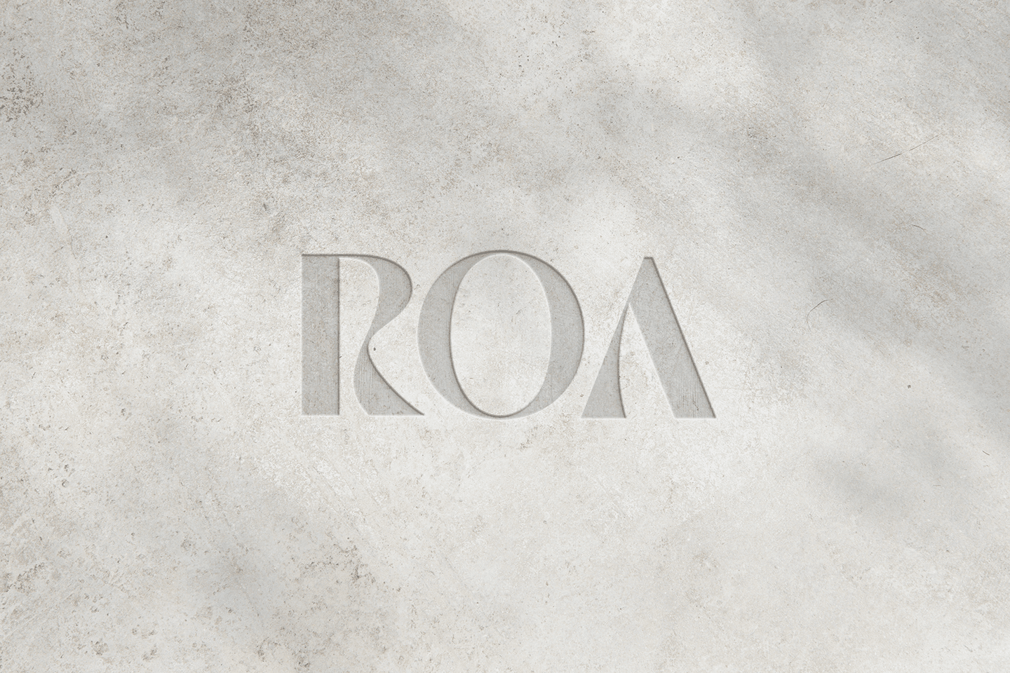 The letters ROA are carved or printed in a modern font on a light grey, textured concrete surface with soft shadow patterns.