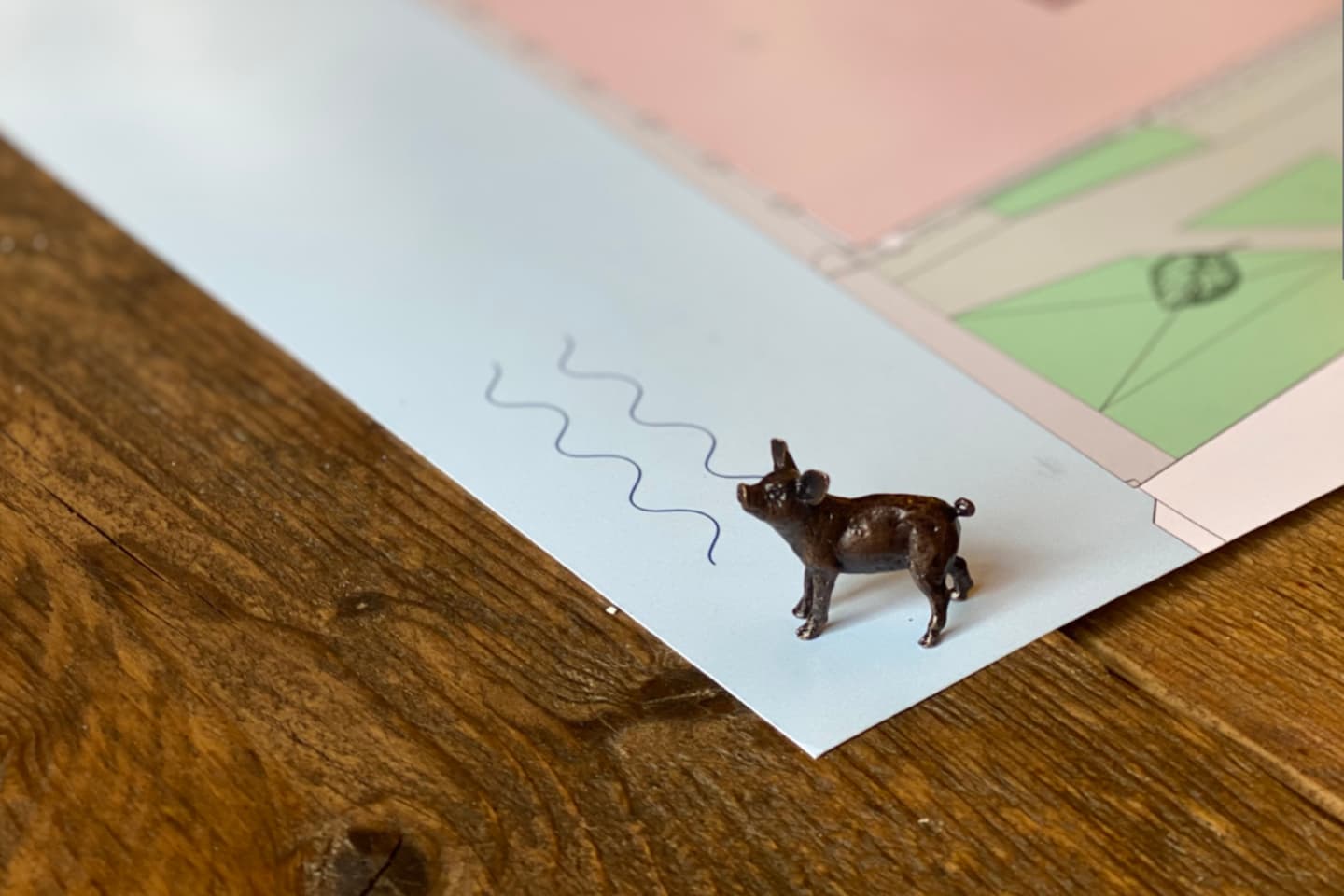 A small toy pig stands on a map near three blue wavy lines, with the map partially covering a wooden surface.