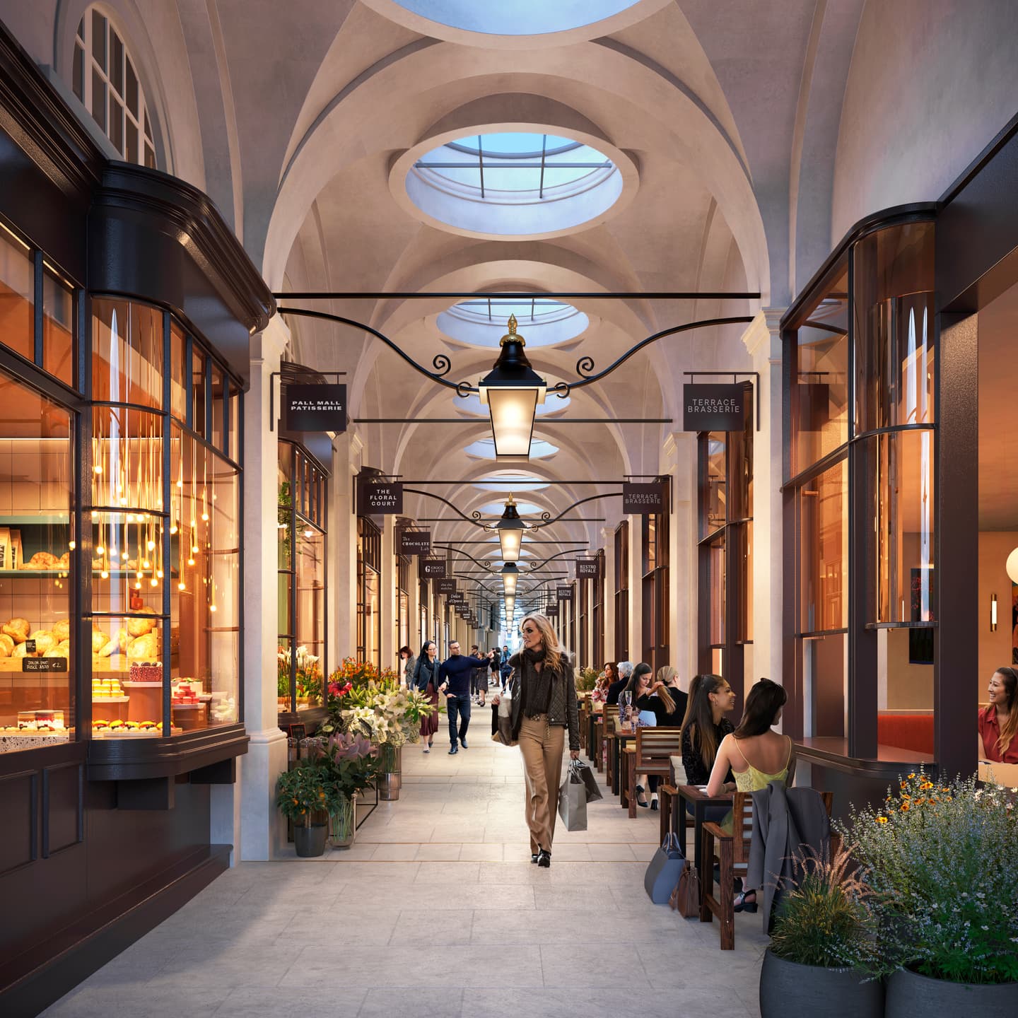 An indoor shopping arcade with arched ceilings, glass shopfronts, people dining at outdoor tables, and shoppers walking along the corridor.