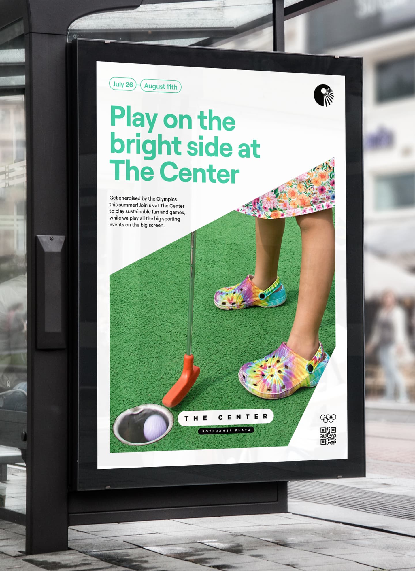 A person in colourful clothing and tie-dye clogs putts a golf ball on green turf; poster text promotes sports events at The Centre from 26 July to 11 August.