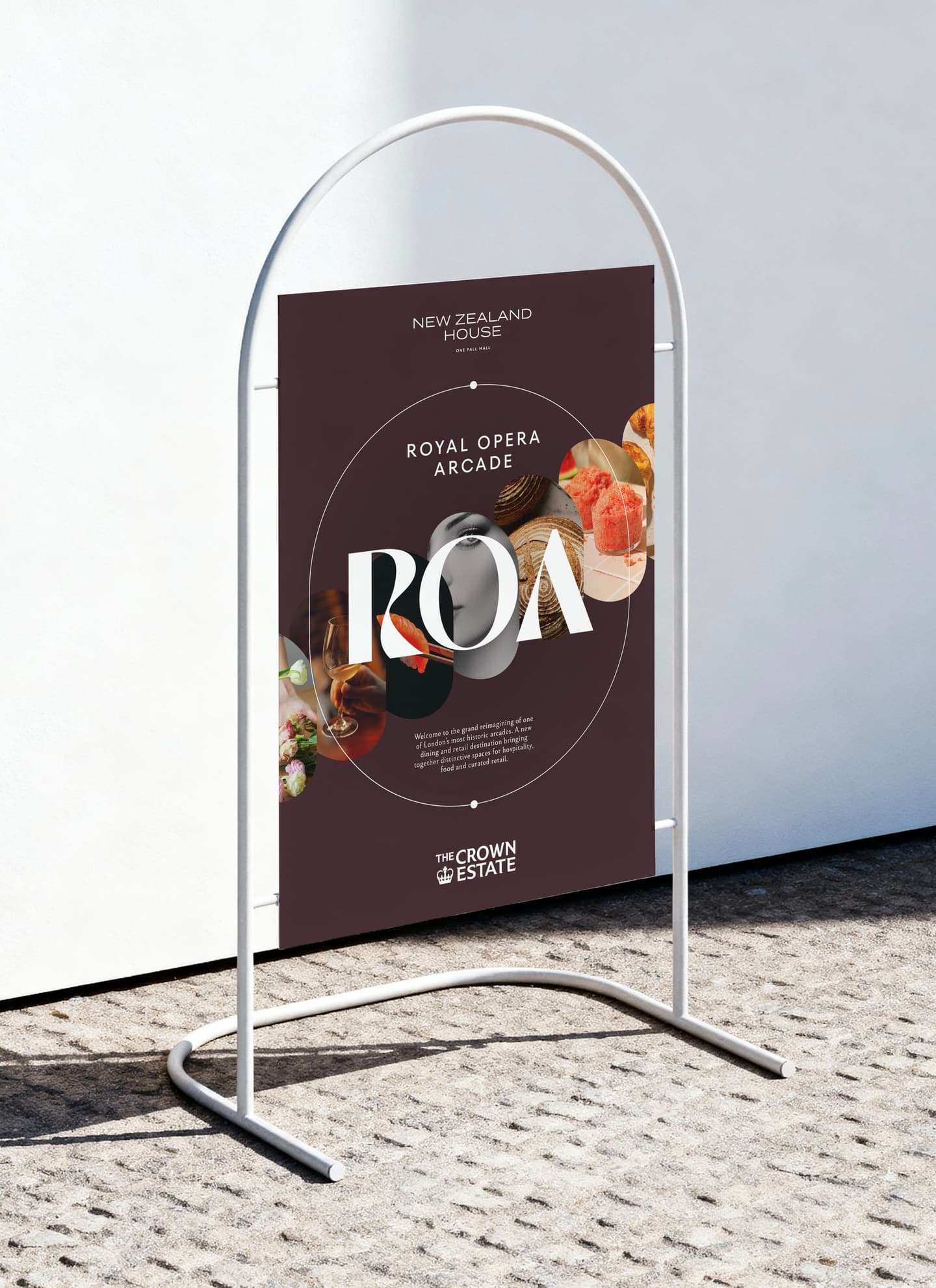 A freestanding sign displays a Royal Opera Arcade event poster with food images and modern graphics against a white wall on a stone surface.