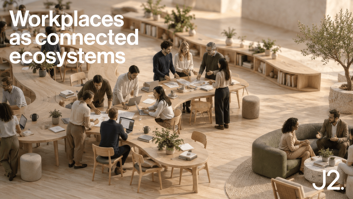 Open office space with people working at tables, holding discussions, and collaborating in a modern, plant-filled environment. Text reads: Workplaces as connected ecosystems.