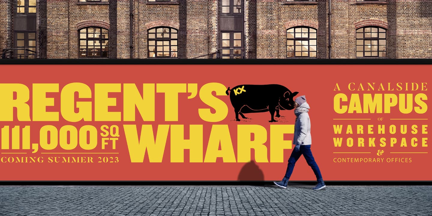 A person walks past a bright Regents Wharf billboard advertising 111,000 sq ft of workspace, opening summer 2023, with bold yellow and black text on an orange background.