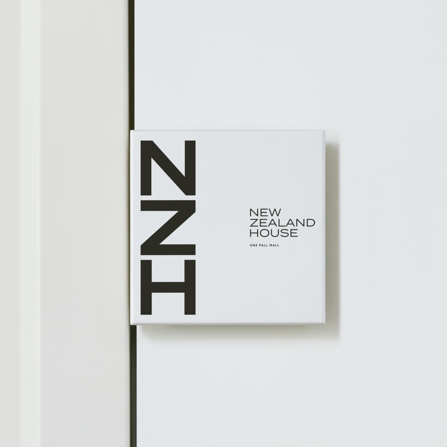 A white square sign on a white wall reads N Z H vertically on the left and New Zealand House One Pall Mall in smaller text on the right.