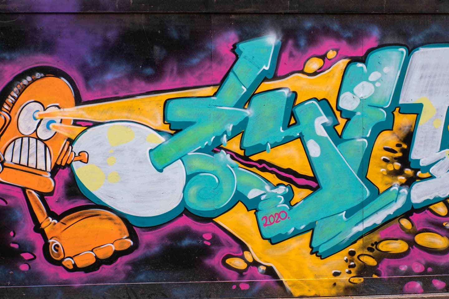 Colourful graffiti features an orange robot shooting a yellow laser at blue letters on a wall with a purple and yellow background.