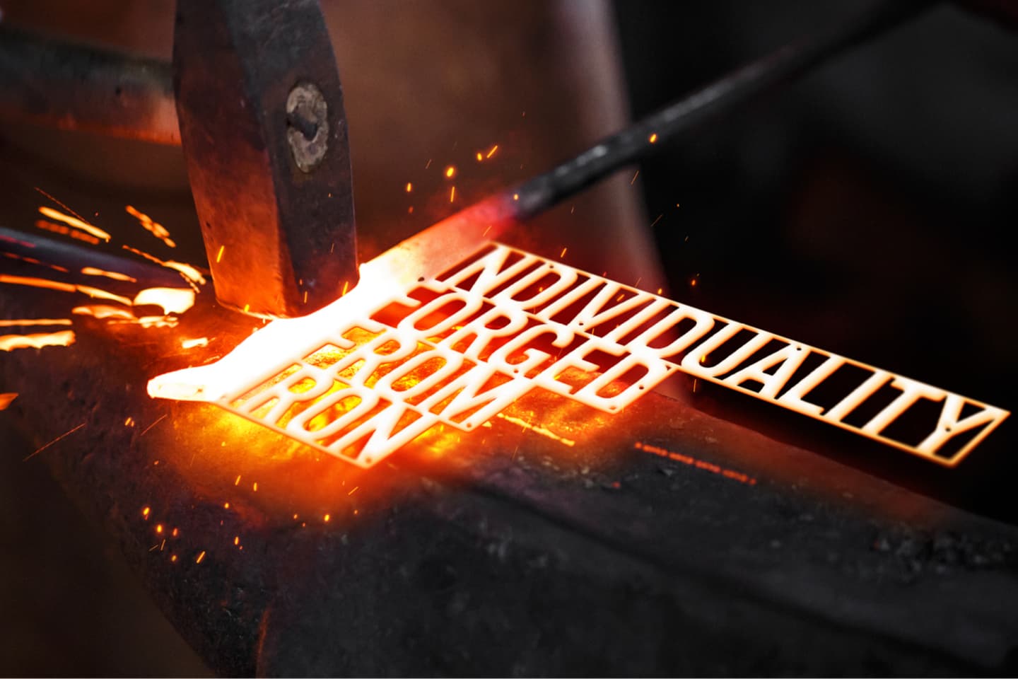 A glowing piece of iron being hammered on an anvil with the words INDIVIDUALITY FORGED FROM IRON cut out, surrounded by flying sparks.