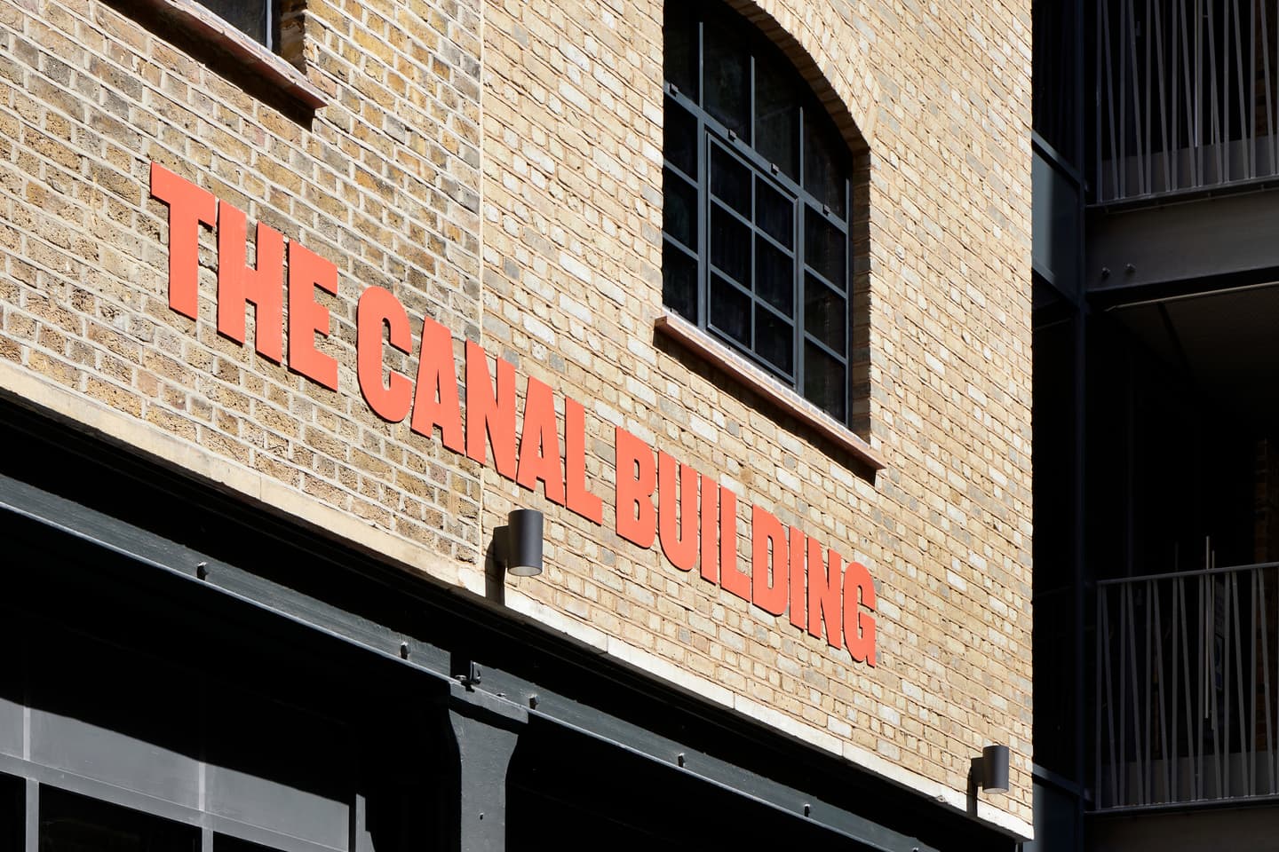 Exterior of a brick building with large orange letters reading THE CANAL BUILDING mounted on the wall below a window.
